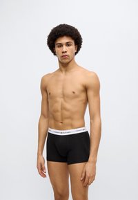 Μαύρα ανδρικά εσώρουχα boxer με λευκή ελαστική μέση που φέρει το λογότυπο "TOMMY HILFIGER". Λείο ύφασμα, εφαρμοστή γραμμή και μήκος έως τη μέση του μηρού.