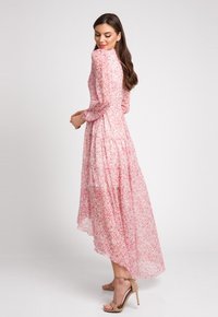 Maxi sukienka z przezroczystego różowego materiału z drobnym kwiatowym wzorem, długimi rękawami, wysokim dekoltem, warstwową spódnicą i subtelnym falbaniastym dołem.