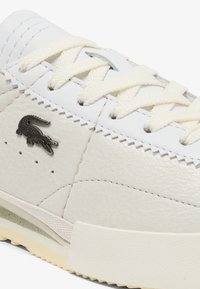 Białe skórzane sneakersy z kremowymi sznurowadłami, charakteryzujące się fakturowaną powierzchnią i ciemnym logo. Niskoprofilowy design z mi ękką gumową podeszwą.