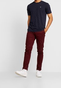 Marine t-shirt med hvide og lyserøde prikker, parret med bordeaux slim-fit bukser og hvide sneakers. Enkel, afslappet outfit.