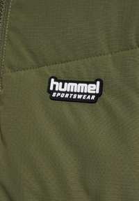 Olivgrön sportjacka med en texturerad tyg, diagonala sömmar och en svartvit "hummel SPORTSWEAR" logotyp.