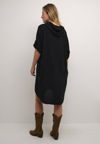 Rochie neagră cu glugă, mâneci răsfrânte, croi lejer și tiv înalt jos. Fabricată dintr-un material ușor, cu un aspect texturat.