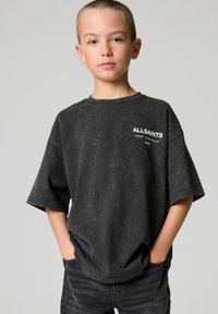 Černé oversized tričko s drsnou texturou, krátkými rukávy a bílým logem "ALLSAINTS" na hrudi. V kombinaci s tmavými džíny.