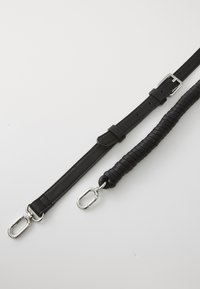 Crne kožne trake, jedna glatka s kopčom, a druga teksturirana s uvijenim dizajnom; obje imaju metalne kopče.