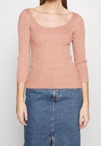 Prążkowany, jasnoróżowy top z długim rękawem i dekoltem typu scoop. W połączeniu z dżinsową spódnicą z przednim rozcięciem. Gładka tekstura i dopasowany krój.