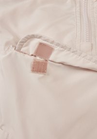 Tissu rose clair avec une texture lisse, comportant une fermeture éclair et deux patchs en Velcro à l'intérieur, présentant un design minimaliste.
