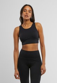 Svart crop-top med rund hals, laget av glatt og elastisk materiale. Den har en tettsittende design og passer godt sammen med høyhåndet leggings.
