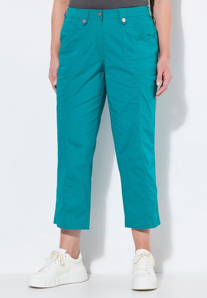 Pantaloni cropped turchesi in un tessuto leggero con due tasche frontali, dotati di chiusura con zip e bottone, abbinati a sneaker bianche.