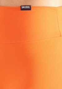 Leuchtend orangefarbene Leggings mit einer glatten, elastischen Textur. Verfügt über ein schwarzes Etikett am Bund. Einfaches, nahtloses Design ohne Muster.