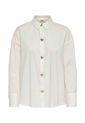 Blouse blanche à manches longues avec col pointu et boutons dorés en forme de cœur sur le devant.