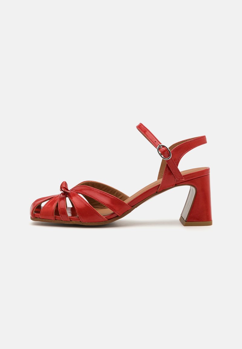 Czerwone skórzane sandały z otwartym noskiem, z krzyżującymi się paskami, węzełkiem z przodu oraz średnim słupkiem z metalicznym akcentem.
