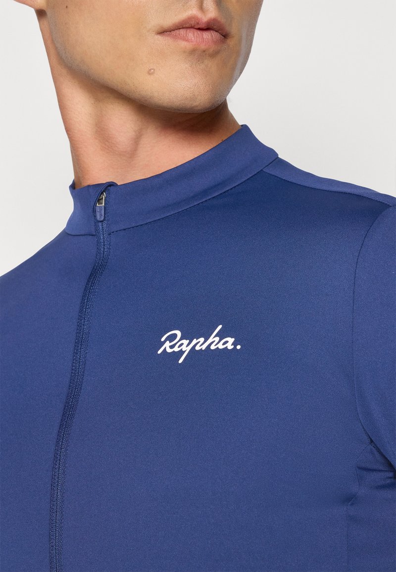 Marineblå cykeltrøje med høj krave, prydet med et hvidt "Rapha" logo, lavet af et glat, strækbart stof med lynlås foran.