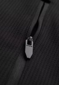 Tessuto nero con zip e motivo testurizzato. Il tirazip presenta un design elegante con il marchio "ombre". La vista ravvicinata mette in evidenza i dettagli del materiale.