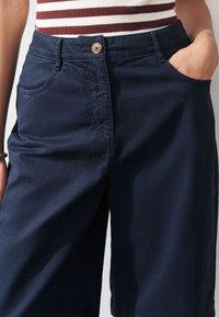 Shorts bleu marine avec fermeture à bouton, poches latérales et texture lisse. Le tissu semble durable avec un design propre et simple.