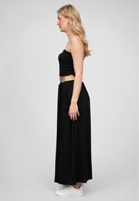 Svart stroppeløs maxikjole med samlet bodice, et beige belte i midjen og hvite sneakers. Glatt stoff og flytende silhuett.