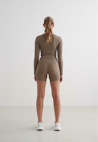 Haut marron à manches longues ajusté avec une texture côtelée, associé à un short taille haute assorti. Le mannequin porte des baskets blanches.