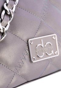 Bolso de mano de cuero gris con textura acolchada en forma de diamante, herrajes plateados y placa con el logo. Cuenta con una correa de cadena y detalles de costuras visibles.