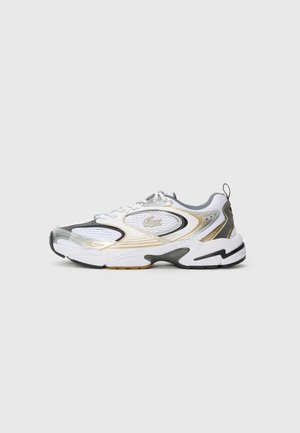 Witte sportieve schoenen met zilveren en gouden accenten, meshpanelen, een ronde neus en een zwarte en gouden zool. Heeft gebogen lijnen en een trekhaak.