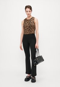 Løveprikket croppet tanktop, svarte brede bukser, svart blank håndveske og kraftige svarte sko. Glatt tekstur og tettsittende design.
