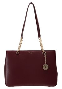 Sac à main DKNY en cuir bordeaux avec des anses en chaîne dorée et un pendentif rond doré avec le logo DKNY suspendu à l'avant.