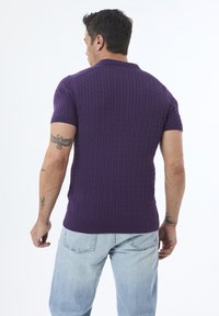 Lilla kortærmet strik polo med kabelmønster, ribbet krave og kant, båret med lyseblå jeans. Vist fra bagenden.