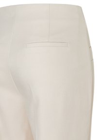 Close-up van beige broek met achterzak met horizontale opening en naaddetails op gladde stof.