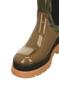 Brown glossy waterproof boot with a rounded toe, black rubber sole, and green accent at the top. Features a textured black fabric panel.