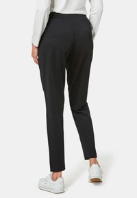 Zwarte slim-fit broek gemaakt van rekbaar materiaal, met een gladde textuur en een hoge tailleband. Gecombineerd met witte sneakers.