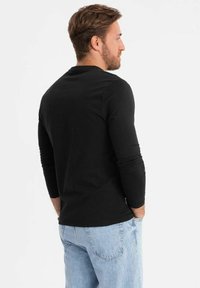 Camicetta nera a maniche lunghe in tessuto morbido, con scollatura rotonda. Abbinata a jeans azzurri chiari, il look è casual e rilassato.