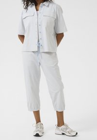 Vaaleansininen raidallinen kaksiosainen asu, jossa on lyhythihainen nappipaitapusero, jossa on kaksi rintataskua, sekä lyhyet narukiristyksellä varustetut housut.