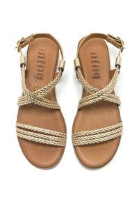 Sandalias con tiras que presentan correas trenzadas doradas sobre una plantilla color topo, con suela plana y un hebilla lateral para ajuste.