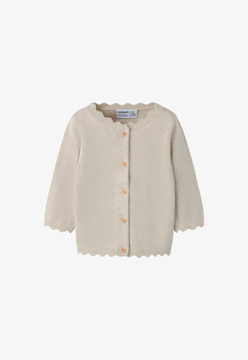Cardigan bébé beige tricoté avec des bords festonnés et des boutons en bois en forme de cœur sur le devant.