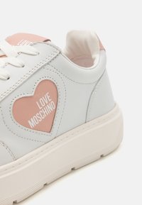 Valged ja heledat roosad tossud nahast ülemise osaga, südamekujuline aktsent ja "LOVE MOSCHINO" valgetes tähtedes. Paksem kummist tall.