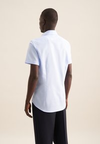 Camicia azzurro chiaro a maniche corte con colletto a punta, linee pulite e una finitura del tessuto liscia; presenta orlo curvo e dettagli minimi.