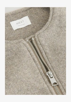 Svetlohnedá vlneno-bavlnená bunda s hladkou textúrou, sietí strieborným zipsom a zaobleným výstrihom, označená nápisom "NEXT" blízko goliera.