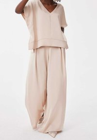 Haut beige ample avec décolleté en V et manches courtes, associé à un pantalon à jambes larges. Tissu lisse et détails de couture subtils.