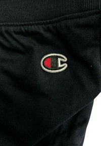 Black fabric showcasing a Champion logo, featuring a red and white emblem, with textured stitching and ribbed material details.