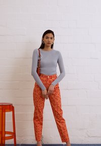 Top de manga longa em cinza claro com textura em nervuras, combinado com calças de cintura alta com padrão de onça laranja. Acessorizado com uma pequena mala castanha.