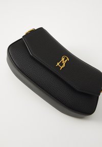 Sac à bandoulière en cuir noir avec une finition texturée, doté d'un matériel logo en ton doré et d'une fermeture à rabat. Forme rectangulaire compacte.