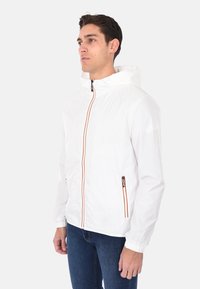 Giacca leggera bianca con cappuccio, zip frontale, due tasche laterali e dettagli della zip arancioni a contrasto. Tessuto liscio e resistente all'acqua.