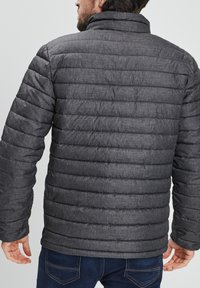 Giacca imbottita in tessuto grigio scuro con motivo trapuntato orizzontale. Presenta un colletto alto e un design leggermente aderente.