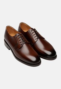 Chaussures en cuir marron avec une finition lisse, bout arrondi et un design à laçage à cinq œillets. Présentent des coutures tonales et un petit talon.