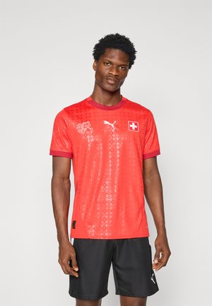 Red short-sleeve soccer jersey with a textured pattern, featuring Puma logo and Swiss flag. Worn with black shorts.