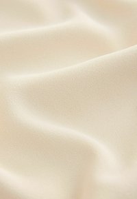 Tejido de color beige claro con una textura suave, un ligero brillo y un sutil patrón granular fino, que muestra suaves pliegues de caídas.