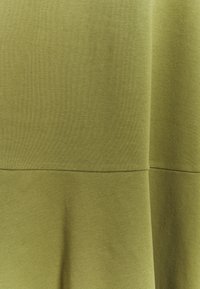 Olivgrön tyg med en slät textur; har en söm som delar upp i två sektioner. Mjukt, elastiskt material med en subtil glans.