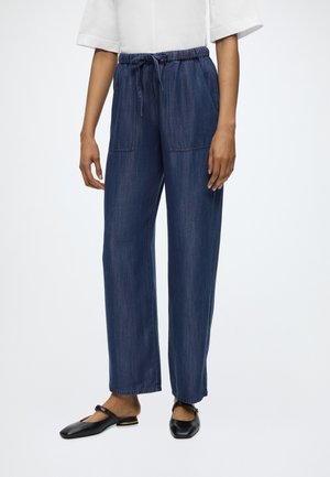 Person wearing loose-fit, elastic waist dark denim pants with front pockets and black flat Mary Jane shoes.