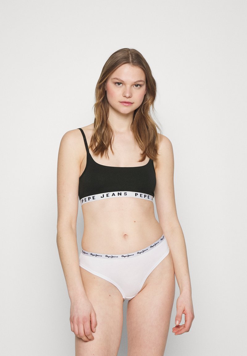 Bralette noire avec bande blanche de marque et sous-vêtements de bikini blancs avec taille logo assortie. Tissu lisse, design ajusté, style contemporain.