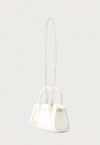 Μικρή λευκή τσάντα χειρός με δύο λαβές και μακρύ ασημένιο λουρί αλυσίδας, σε απλό ανοιχτό φόντο.