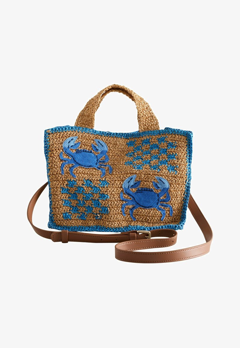 Geweven tan draagtas met blauwe bies, versierd met twee blauwe geborduurde krabben en blauwe geruite patronen, met een bruine leren schouderriem.