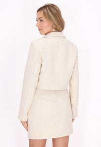 Kreemi värvi tweed bleiser, millele on sobitatud mini seelik. Kangas on tekstuuriga viimistlusega, mille sees on peened metallkiud ja struktureeritud siluett.